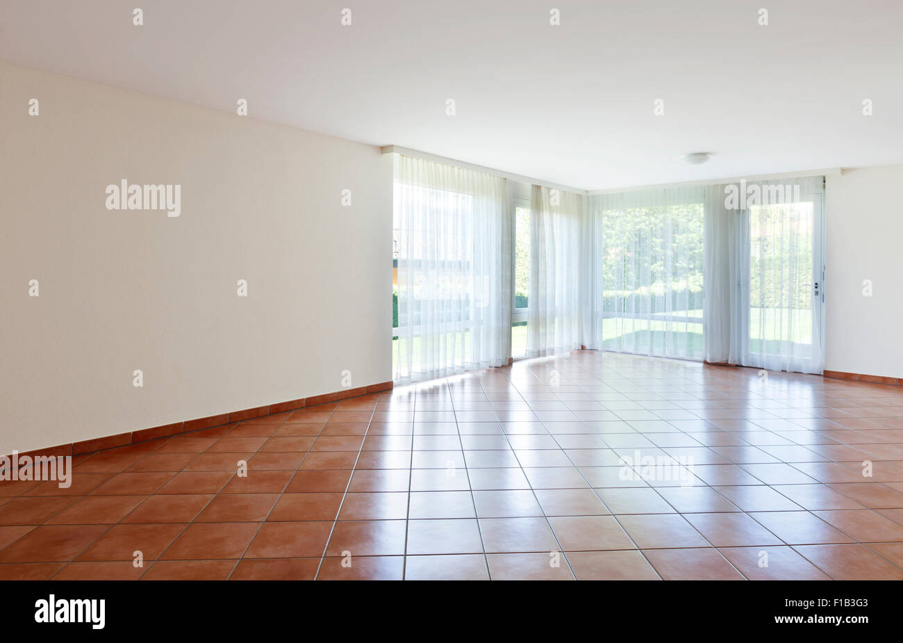 room with terracotta floor,windows with white curtains Stock Photo