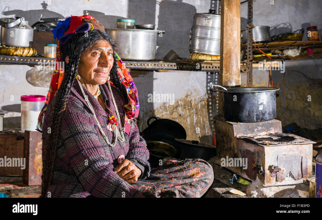 A woman of the Brokpa tribe, working in the kitchen, wearing her traditional dress with the typical flower headdress, Dah Hanu Stock Photo