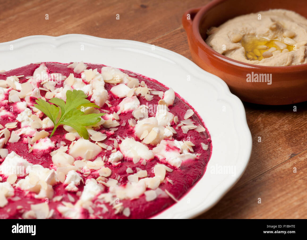 Beetroot puree with za atar spices, yoghurt and garlic garnished with goat's cheese and almonds on a cream plate.  Bowl of hummu Stock Photo