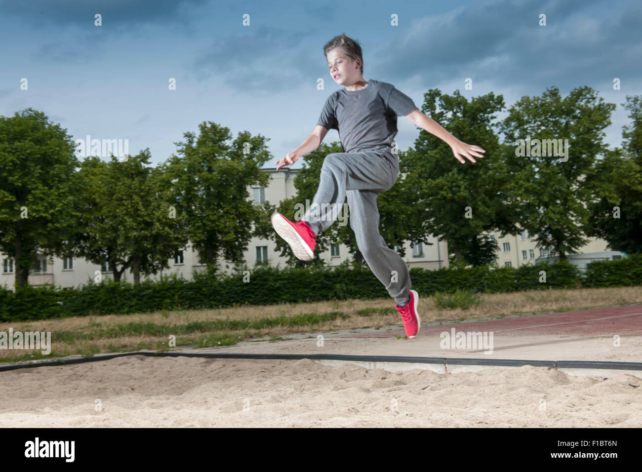 frozen side frontal full body view of a male young teenagers jumping into a long jump pit Stock Photo