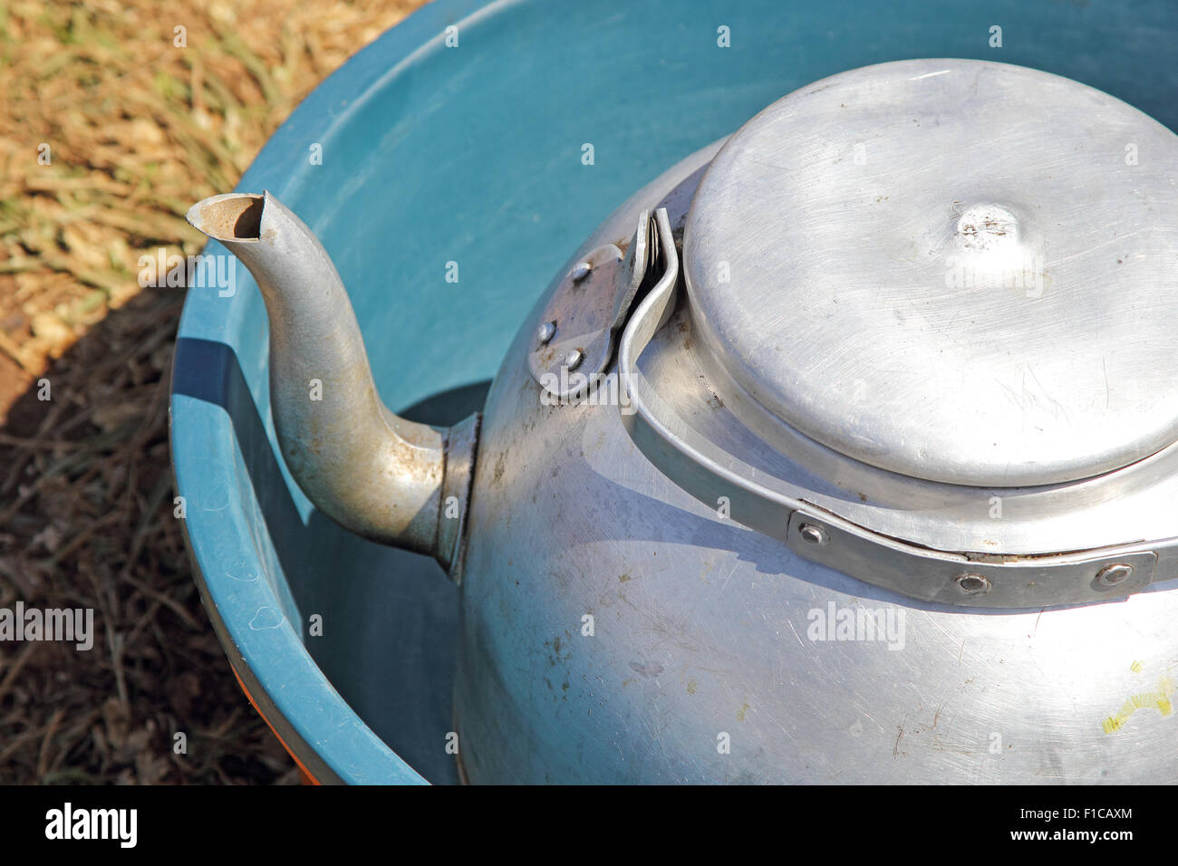 An old iron kettle inside a plastic blue basin, a simple and effective camping equipment for everyday tasks like cooking and was Stock Photo