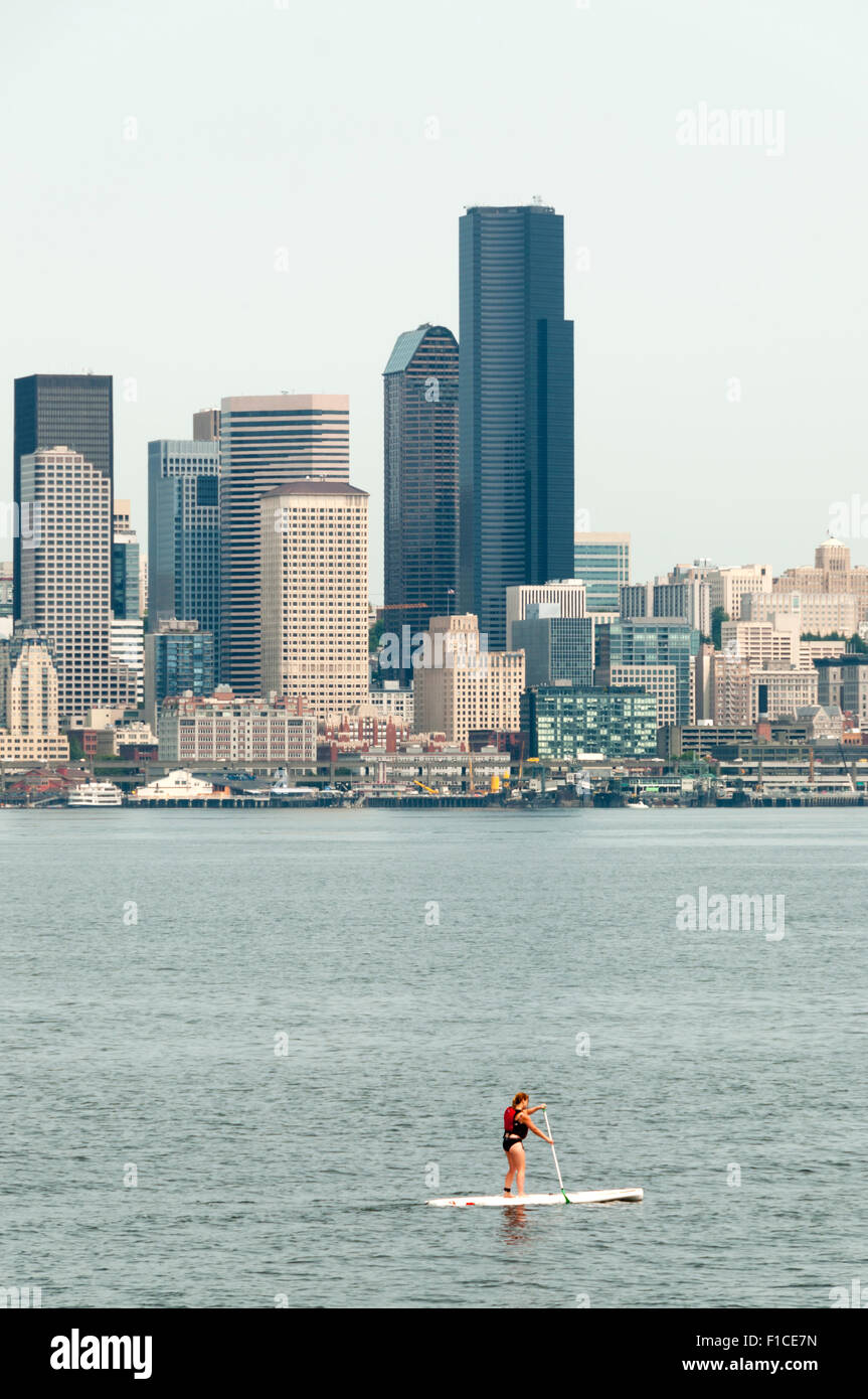A girl paddle boarding across Elliott Bay from Alki Beach with the Seattle skyline in the background. Stock Photo