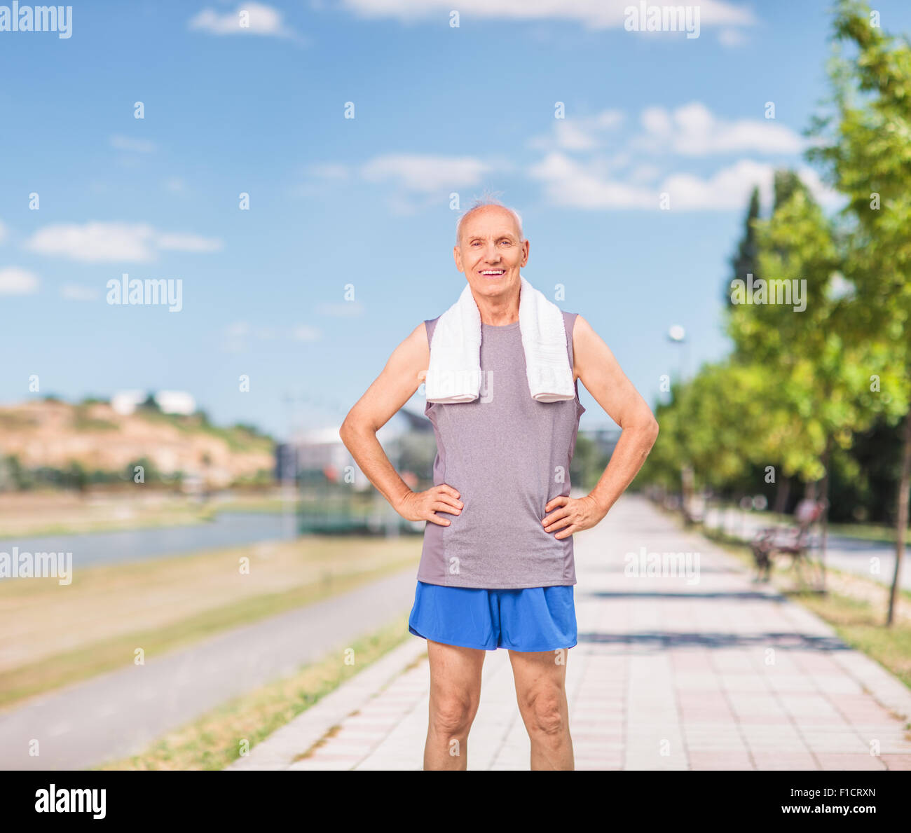 Active senior man in sportswear with a towel around his neck standing on a sidewalk and looking at the camera Stock Photo