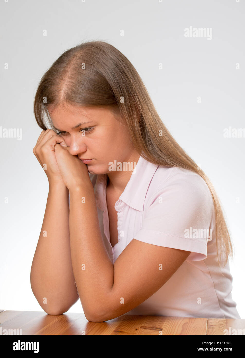 A young sad woman sitting behind a desk, thinking about problem on white background Stock Photo
