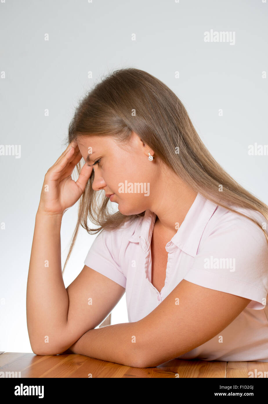 A young tired woman with headache sitting behind a desk and sad on white background, having headache Stock Photo