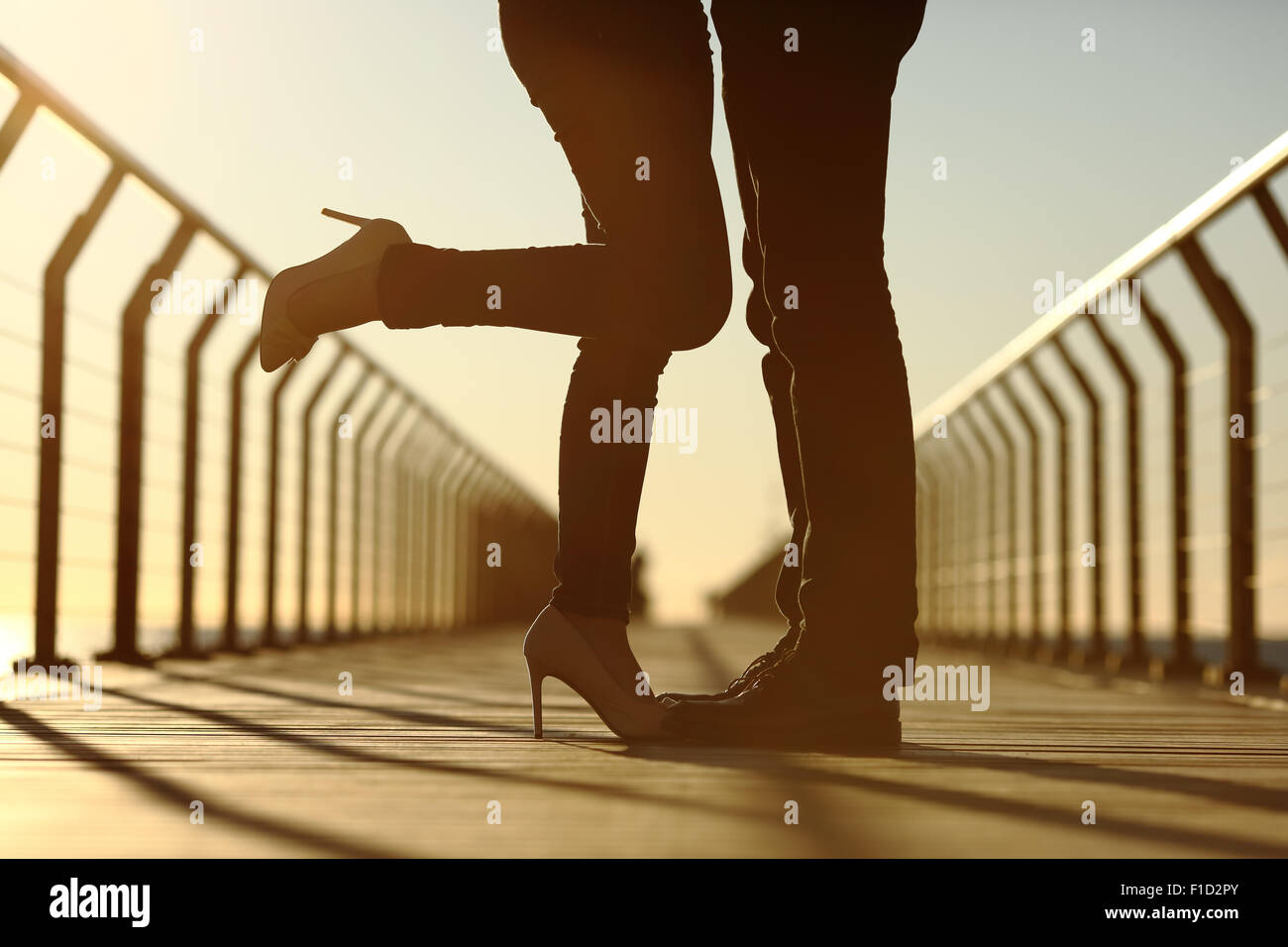 Back light of a couple legs silhouette hugging with love in a bridge at sunset Stock Photo