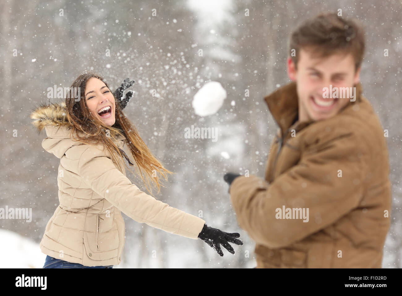 Couple playing with snow and girlfriend throwing a ball in winter holidays Stock Photo