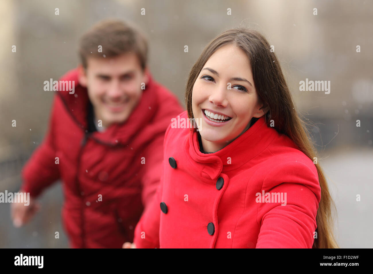 Happy couple wearing red jackets running towards camera in winter Stock Photo