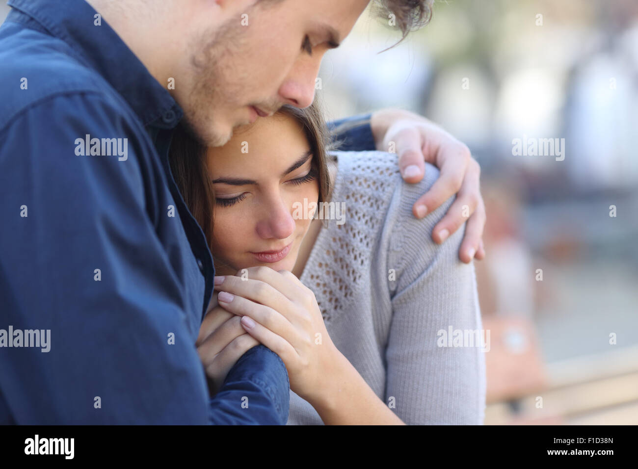 Man comforting his sad mourning friend embracing her in a park Stock Photo