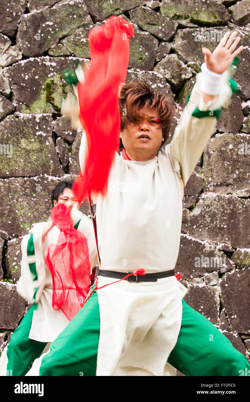 Japanese Yosakoi dance team. Dancers wearing white and green costumes dancing while swirling red cloths. Castle stone wall background. Stock Photo