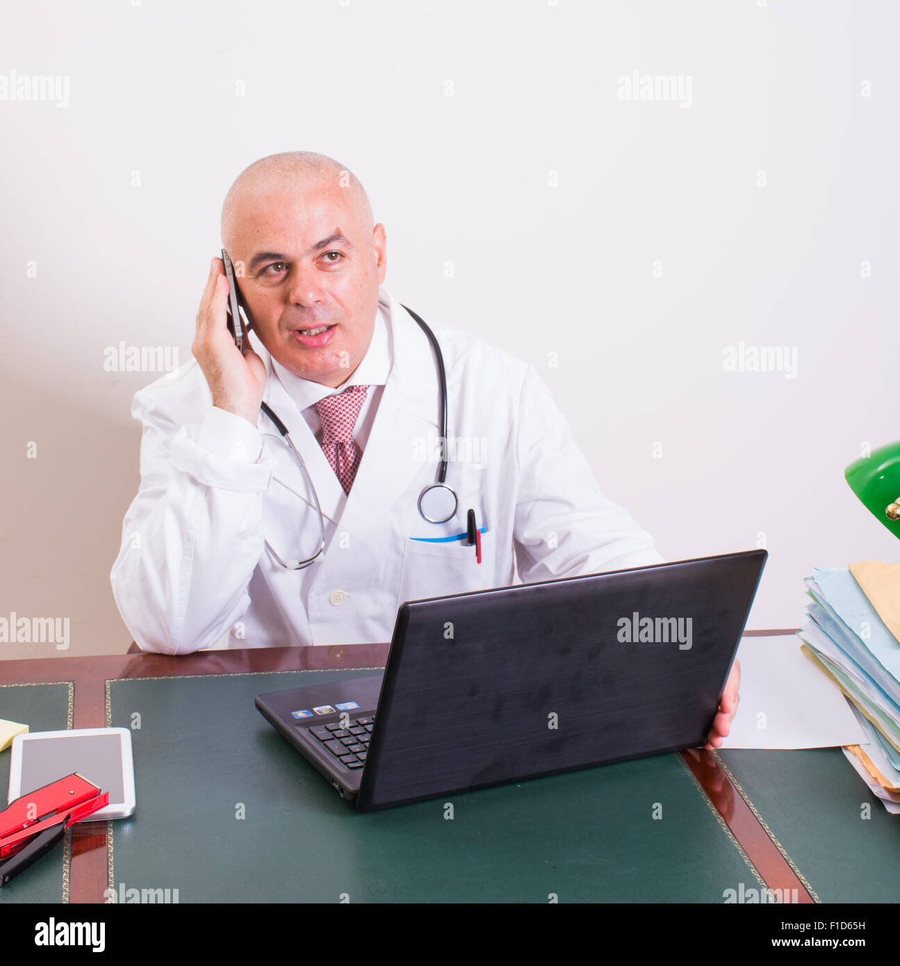 Aback doctor in his studio, uses a smartphone in front of his laptop. Use new technologies. In his professional studio, he is si Stock Photo