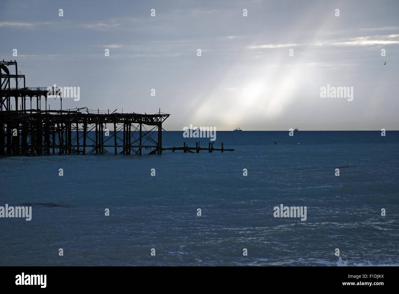 Burnt down remains of West Pier and rays of light on a cloudy sky