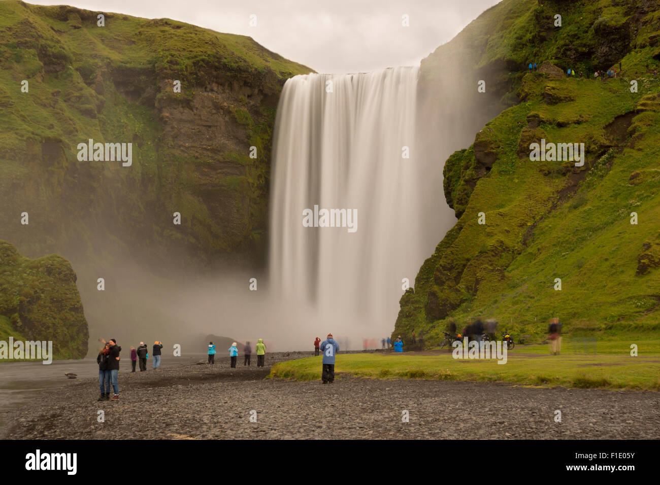 A long exposure of the famous landmark of Skogafoss waterfall on a cold and wet August summer day with tourists below on the south coast of Iceland Stock Photo