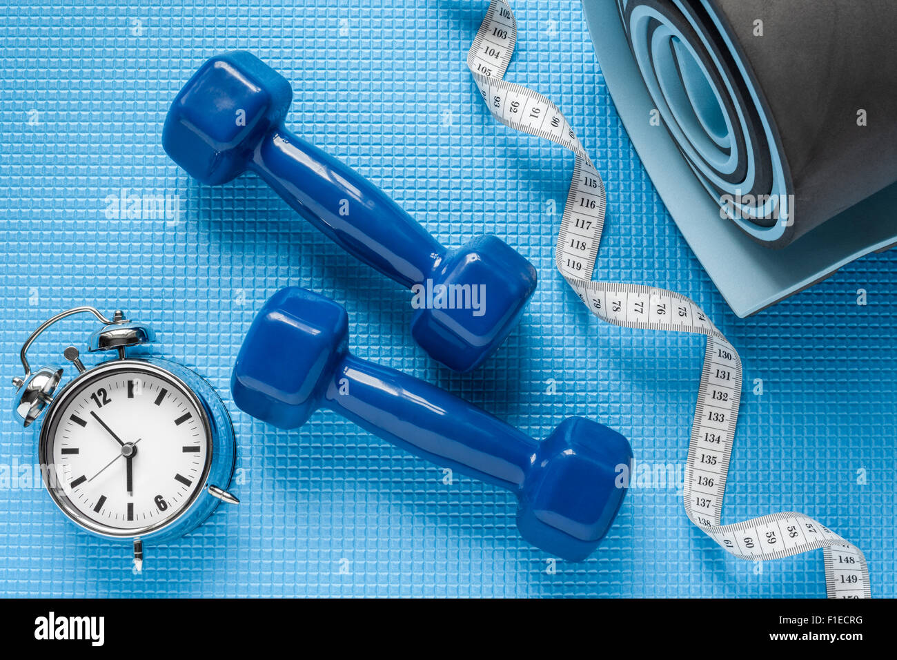 Blue yoga mat, two dumbbells, tape measure and alarm clock. Stock Photo