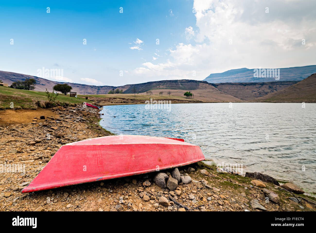Red boat on lake shore with the Drakensberg mountains in the distance Stock Photo