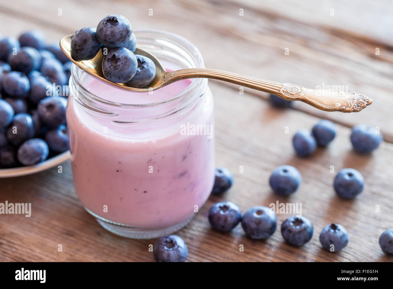 Fresh blueberries yogurt in glass jar, spoon and saucer of bilberries. Stock Photo