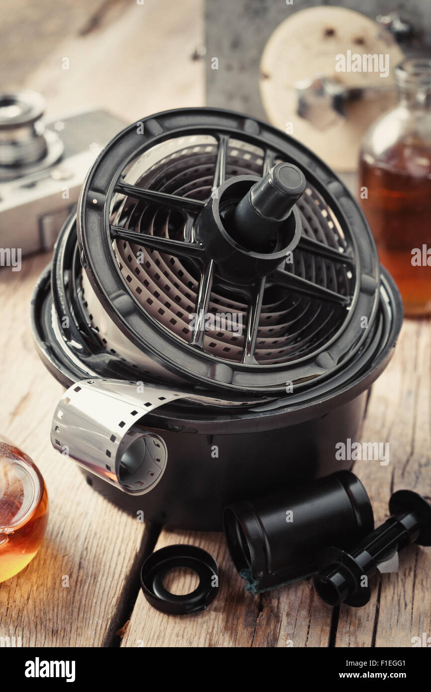 Developing tank with its film reels, photo film rolls, cassette, vintage camera and chemical reagents on desk. Stock Photo