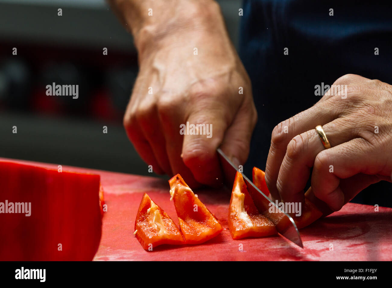 close up of a chefs hands slicing sweet bell peppers on a red cutting ...