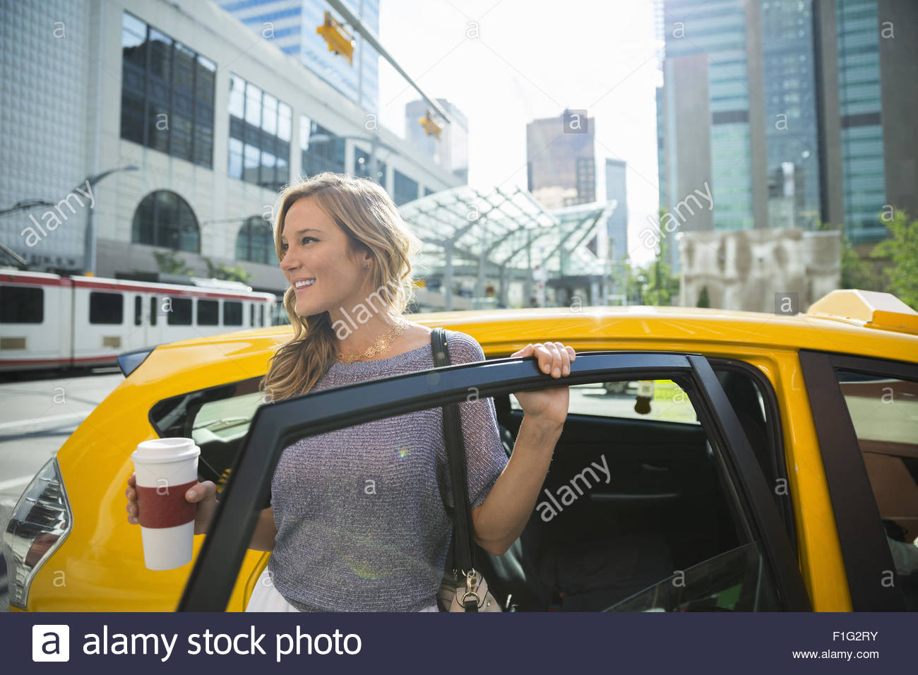 Businesswoman with coffee getting out of taxi Stock Photo