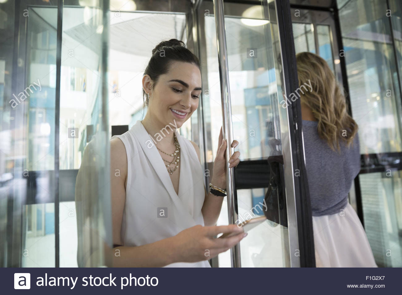 Businesswoman texting with cell phone in revolving door Stock Photo