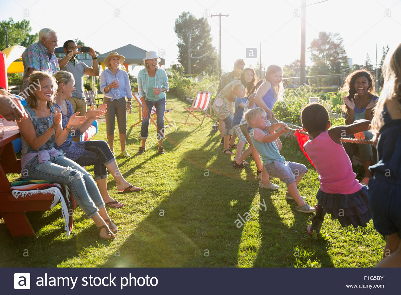Neighbors cheering kids playing tug-of-war Stock Photo