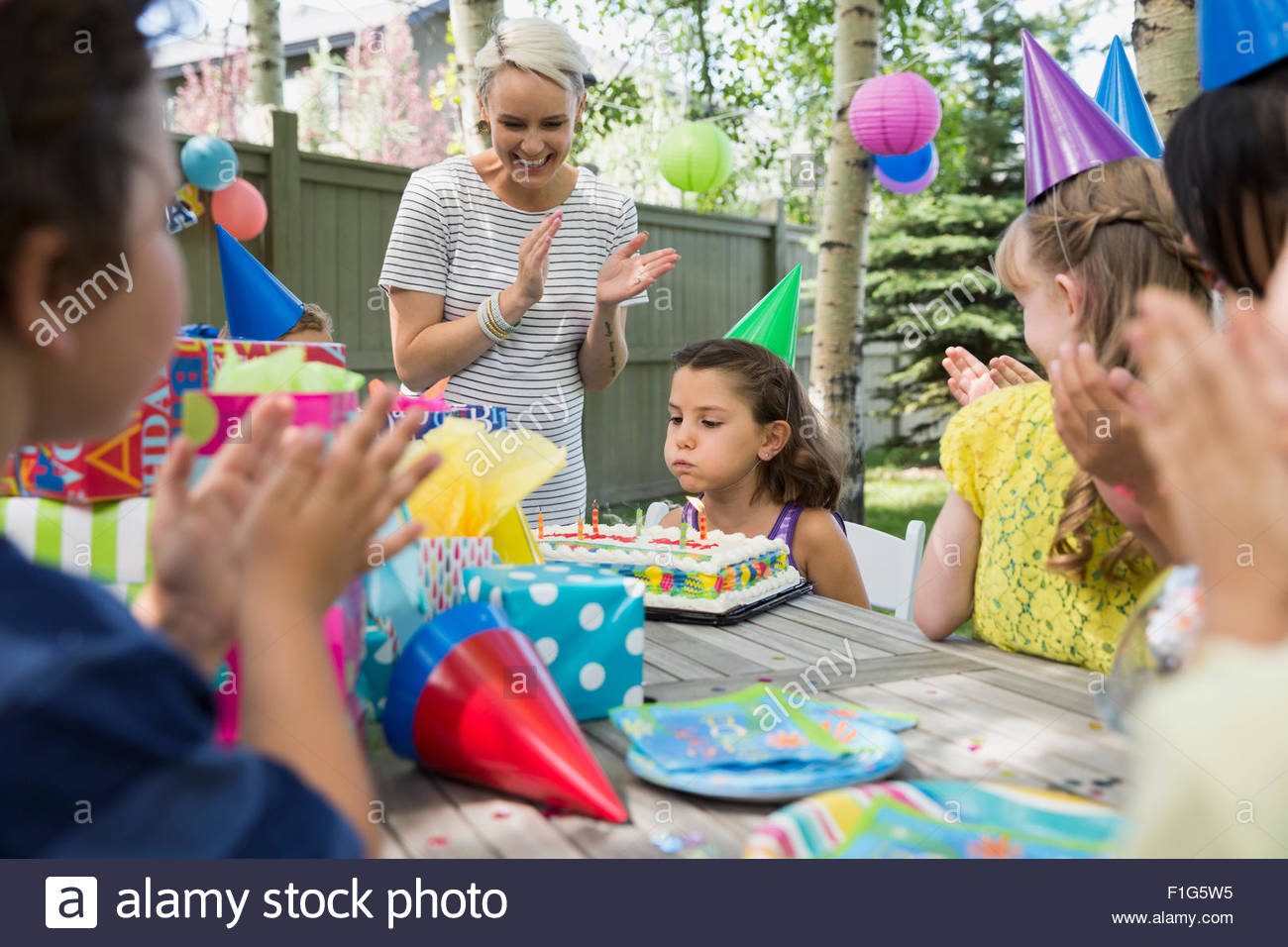 Mother kids clapping for birthday girl blowing candles Stock Photo