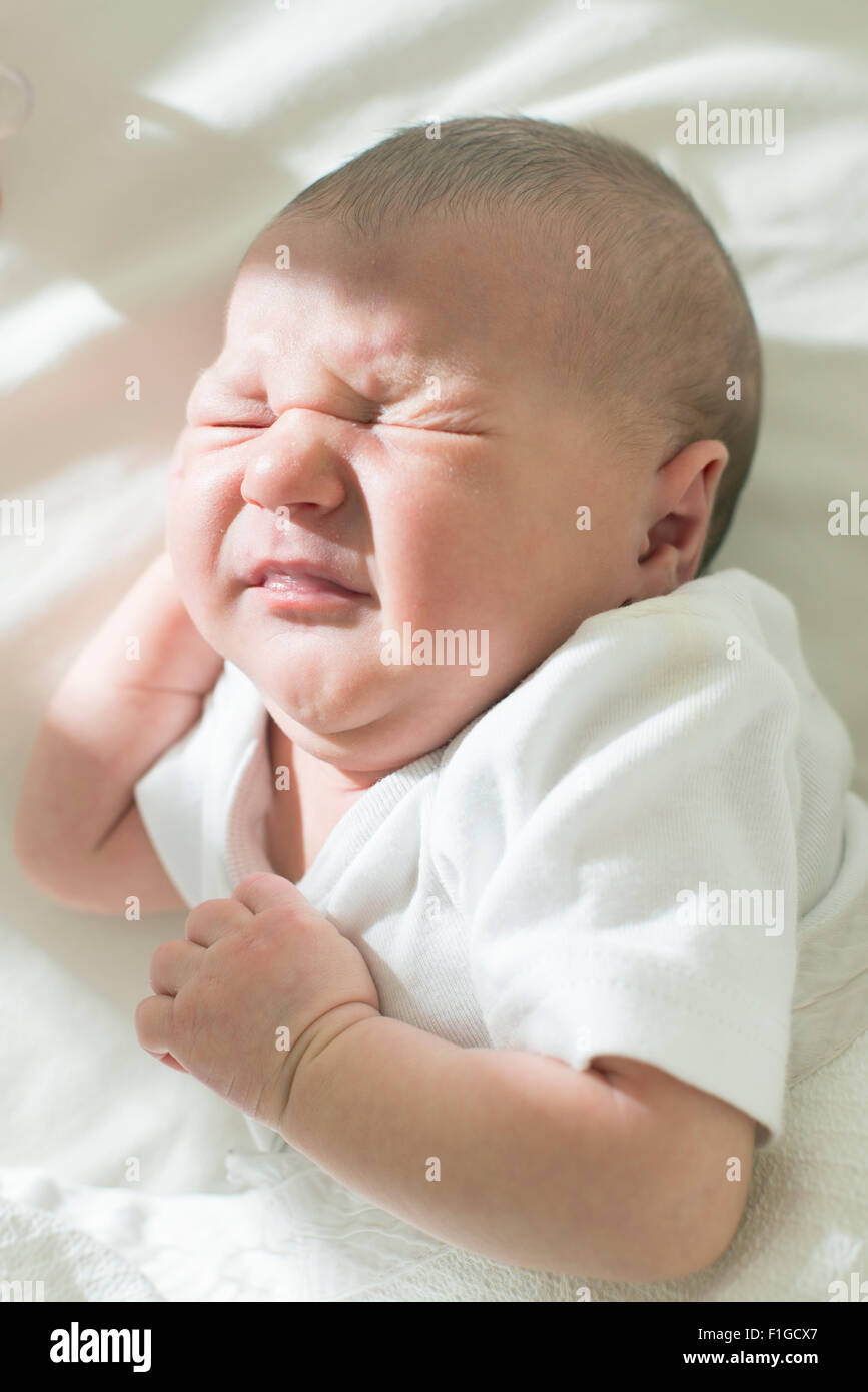 Unhappy frowning baby. White clothes Stock Photo