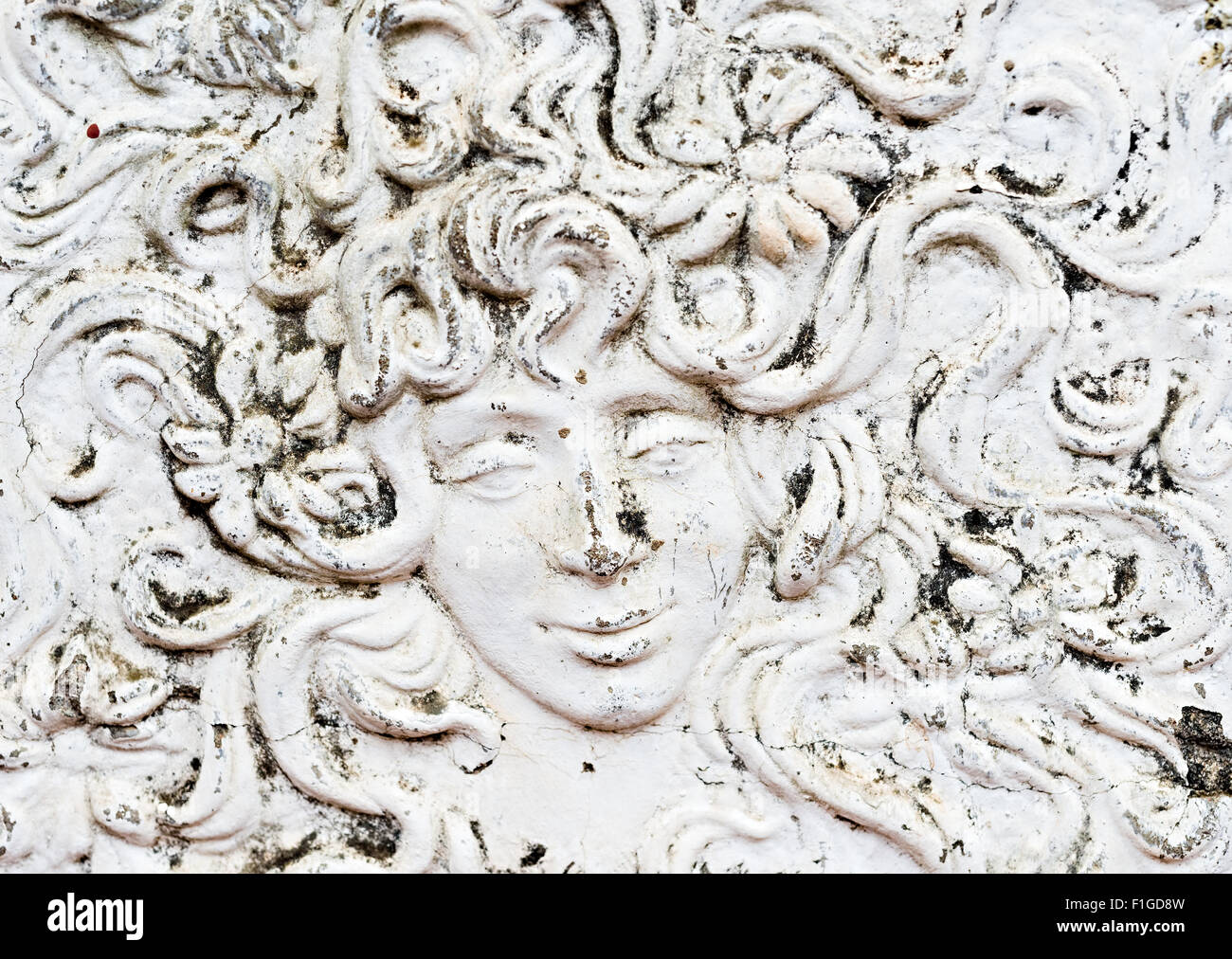 Plaster relief mural of man or woman's face with enigmatic smile and flowers in their hair Stock Photo