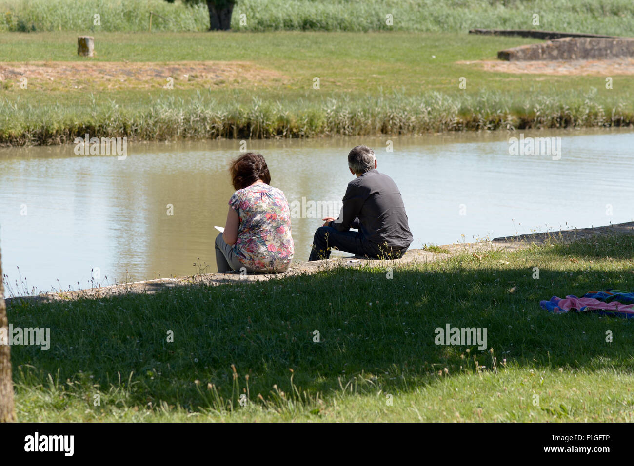 Man And Woman Sat Reading On River Bank At Port Maubert In The Stock Photo Alamy