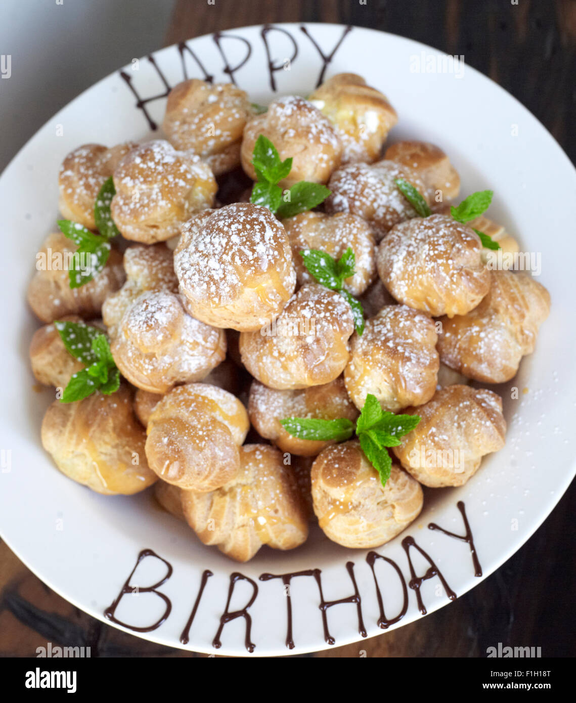 A small profiterole tower, placed in a white bowl with 'Happy Birthday' written onto it in sauce. Stock Photo