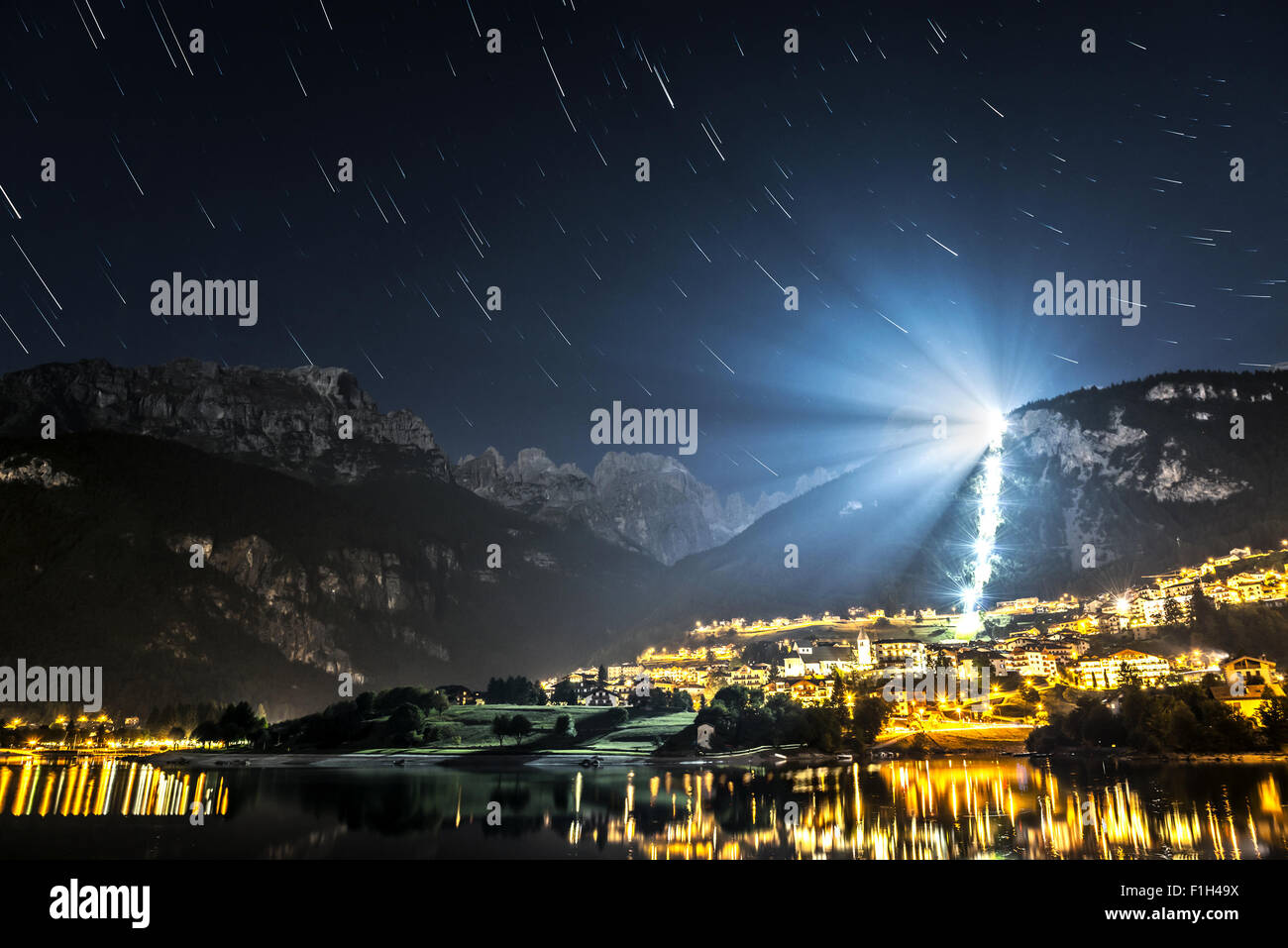Night landscape on the Moveno lake and city with Dolomiti of Brenta Group in background at the moonlight and star trails Stock Photo