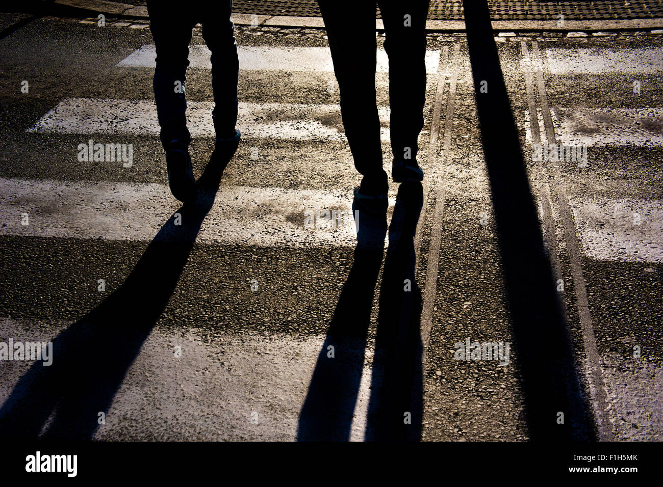 silhouette and long shadows of two persons crossing the street Stock Photo