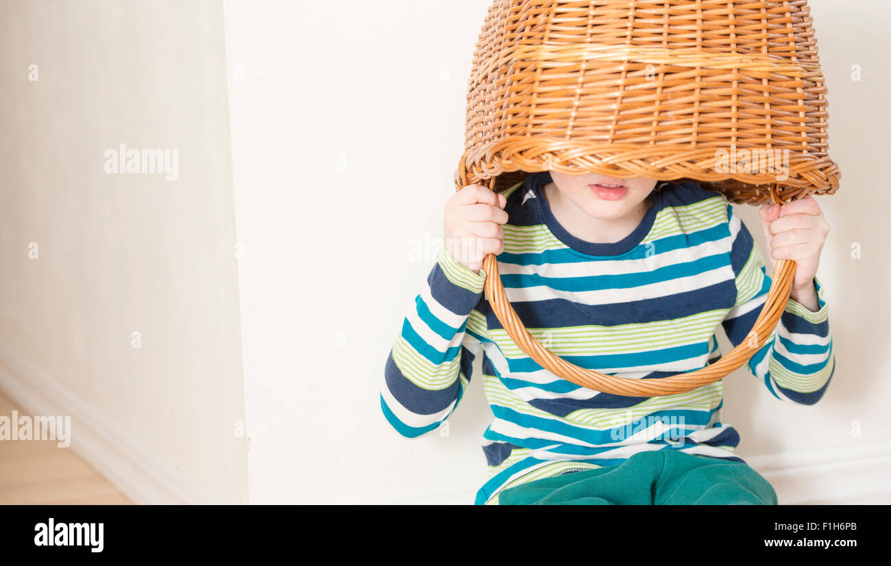 Little girl playing and holding wicker basket over her head. Conceptual image of childhood fun, fantasy and imagination. Stock Photo