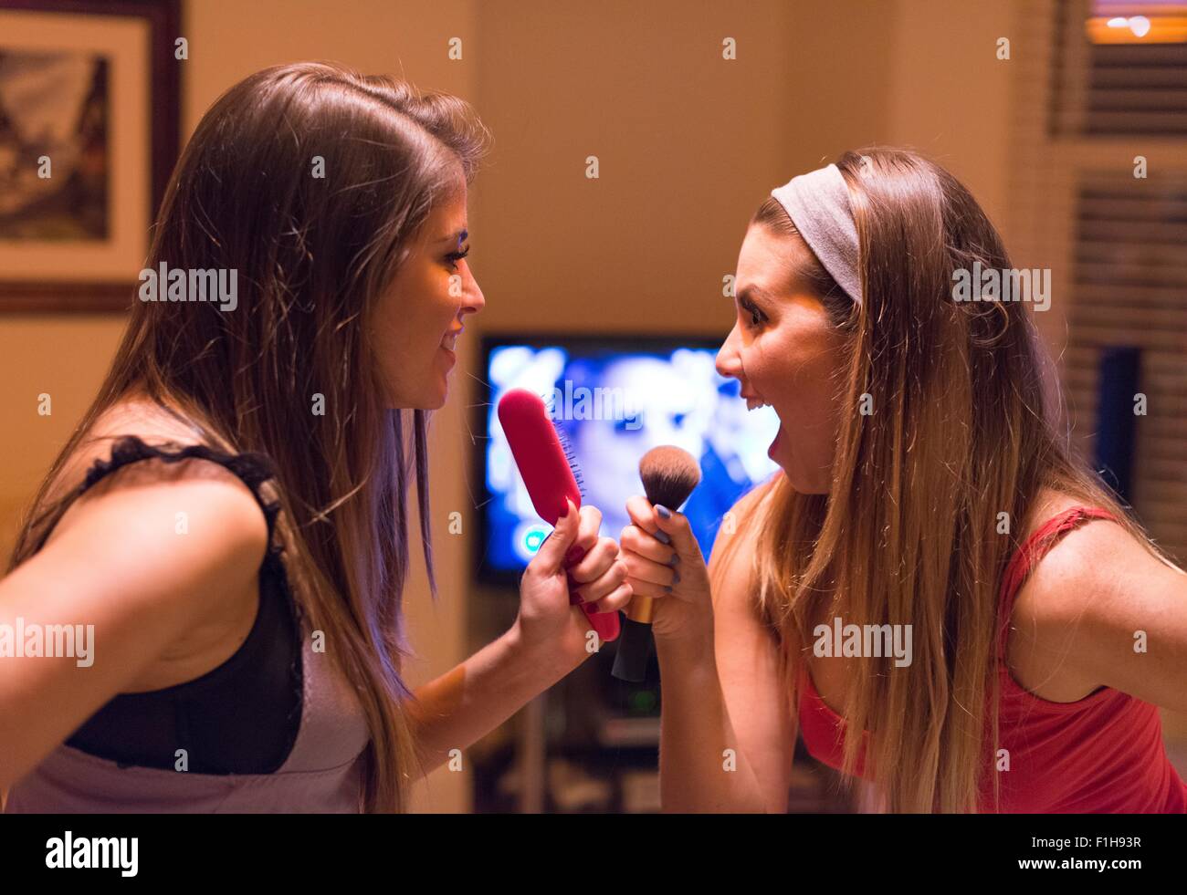 Two young women, singing into hair and make-up brushes Stock Photo