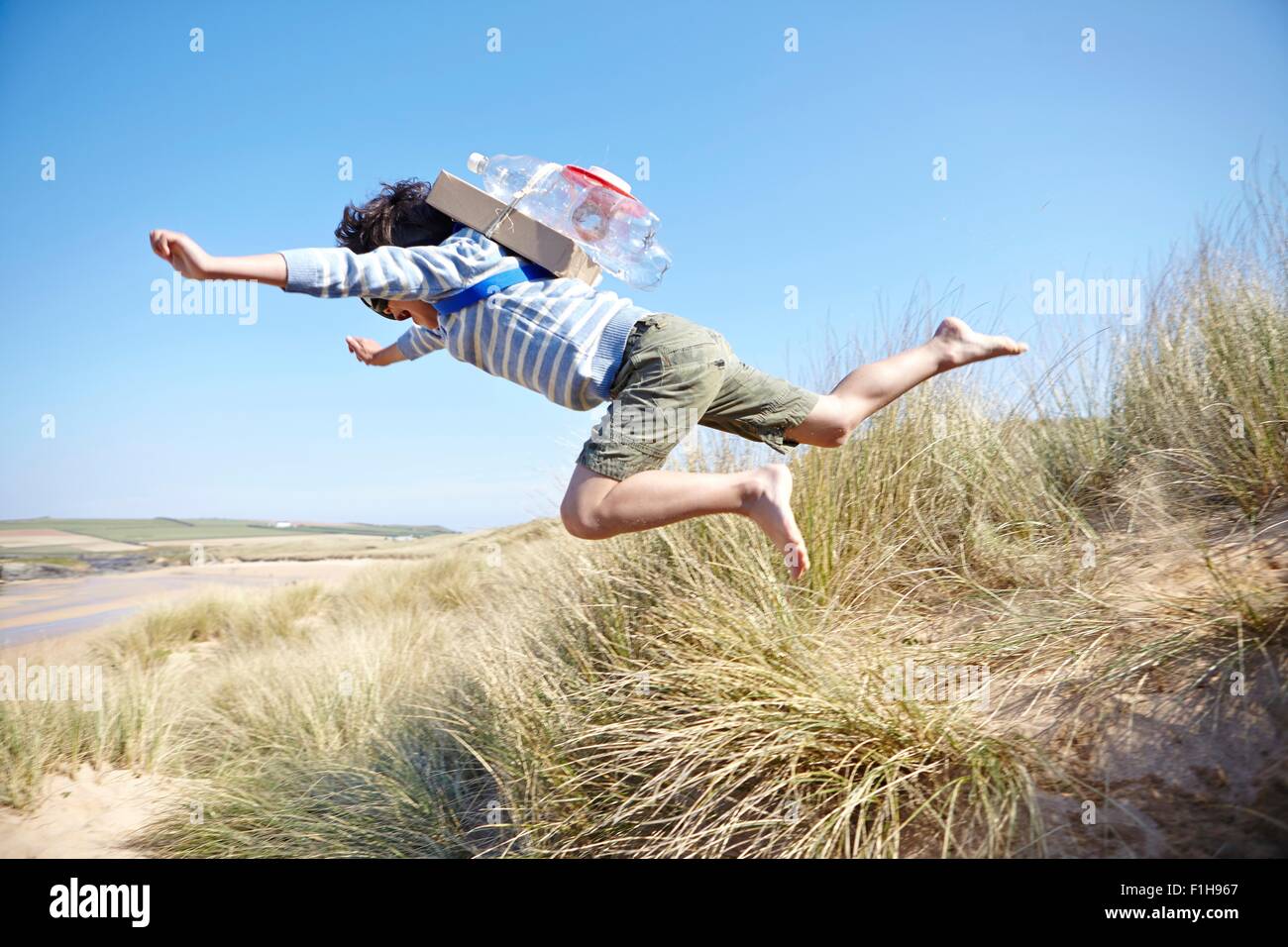 Young boy on beach, wearing fancy dress, leaping into air Stock Photo
