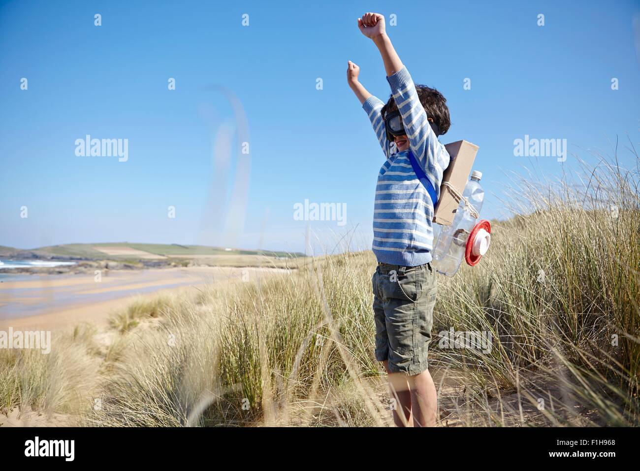 Young boy on beach, wearing fancy dress, arms raised Stock Photo