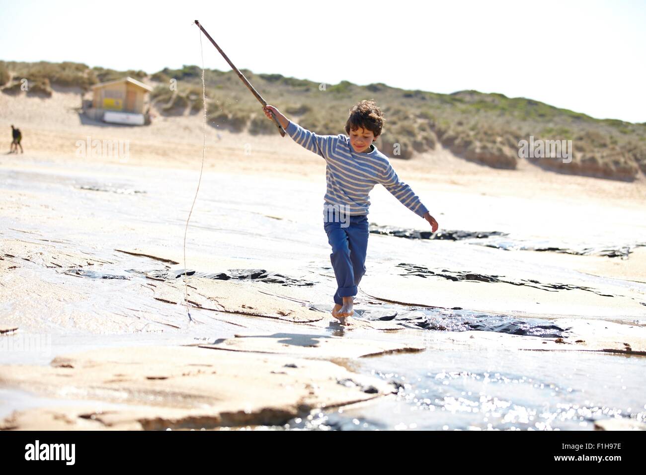 Young boy running along sand with stick Stock Photo