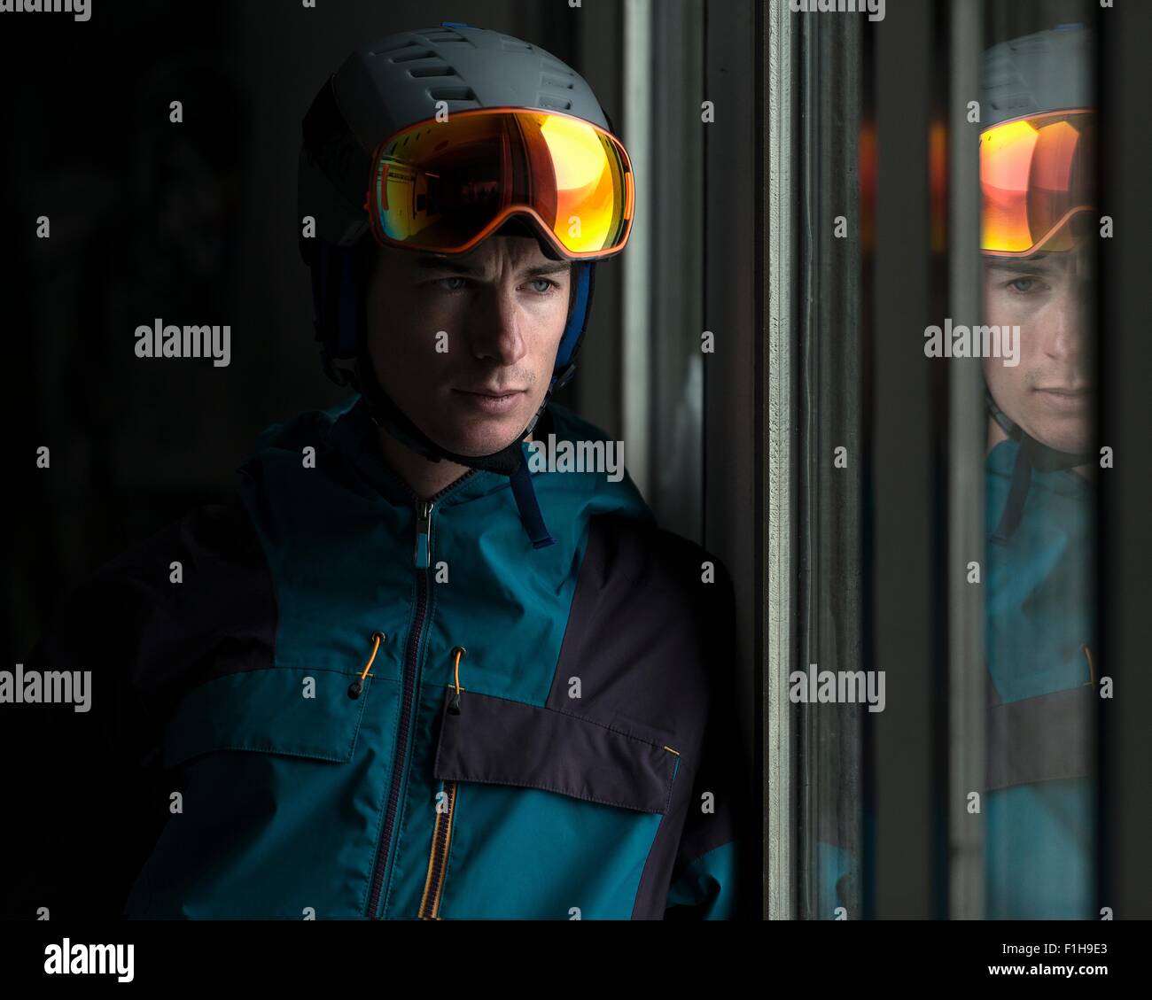 Man wearing helmet and ski goggles looking through window Stock Photo