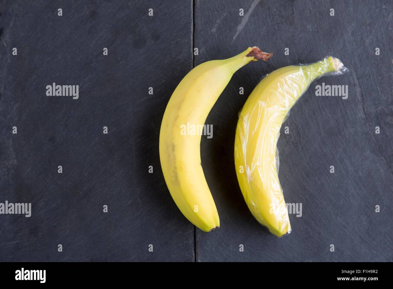 Still life of two bananas - one wrapped in plastic wrap Stock Photo