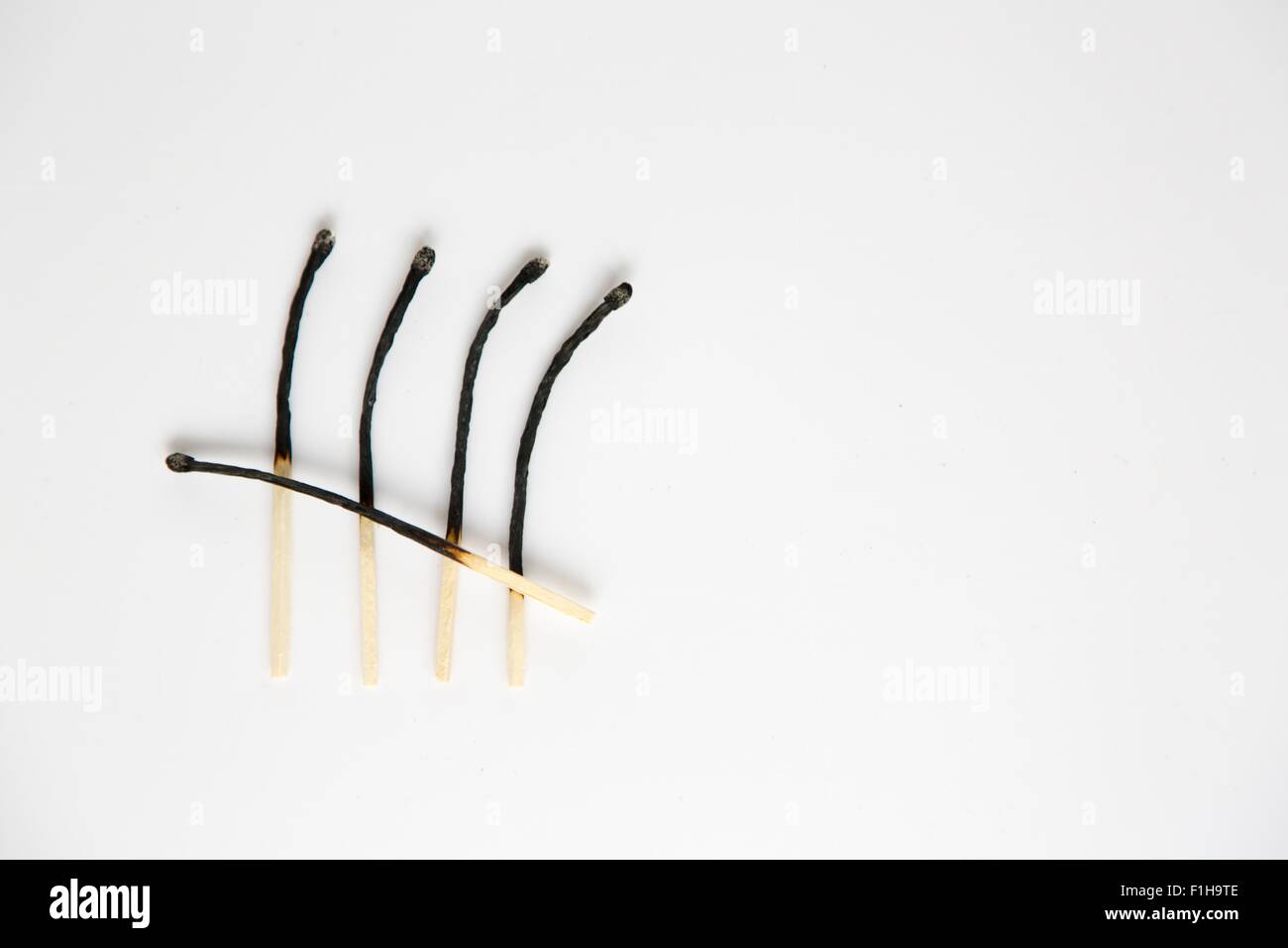 Still life with row of four burnt matches and one across Stock Photo