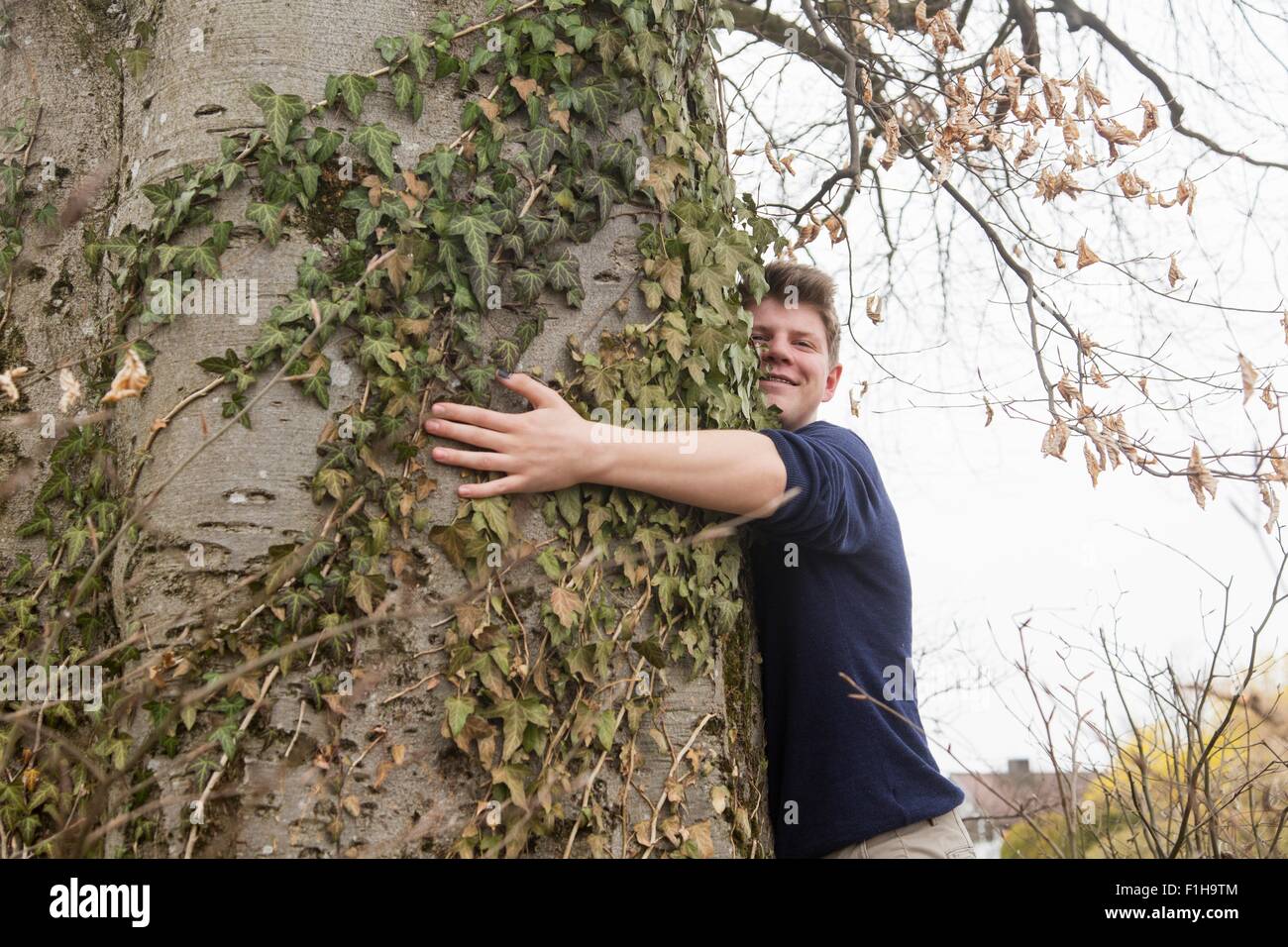 Teenage boy hugging wide tree trunk in garden Stock Photo