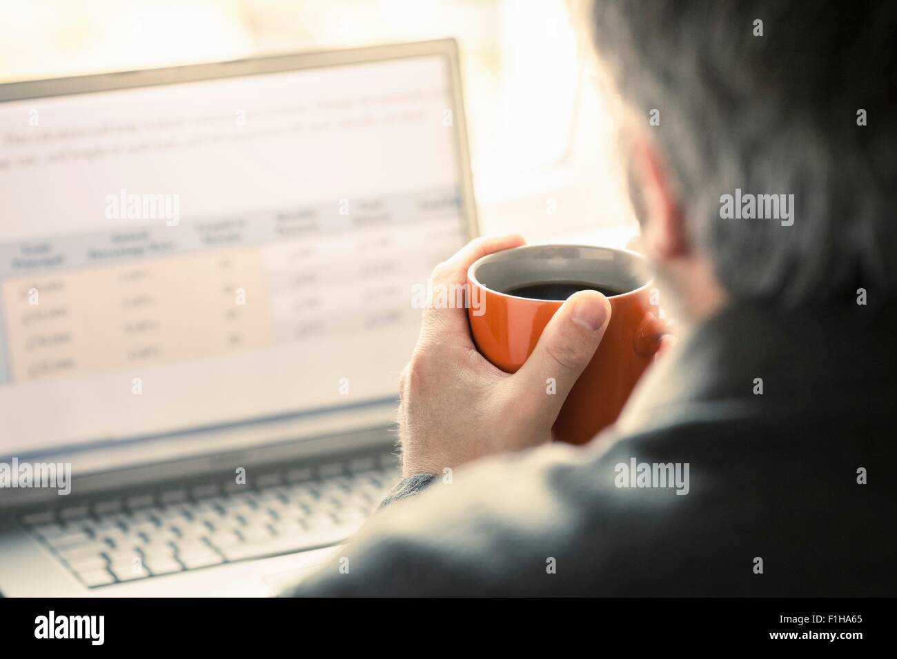 Over shoulder view of man browsing laptop at desk Stock Photo