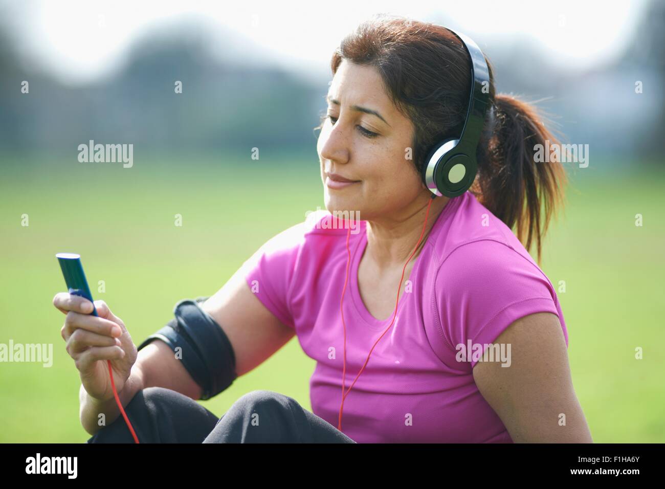 Mature woman taking exercise break in park selecting music from MP3 player Stock Photo