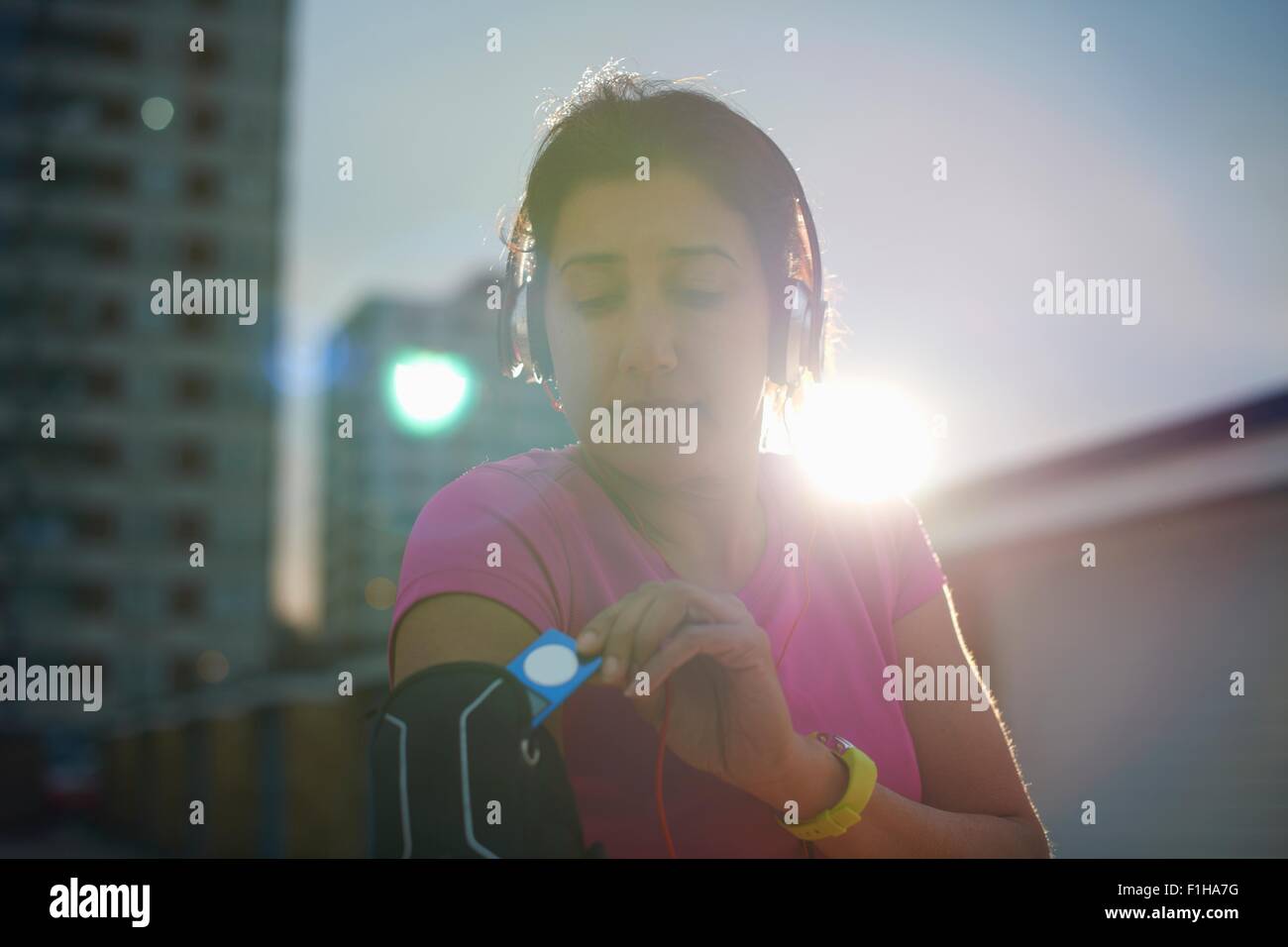 Mature female runner removing MP3 player from armband at dusk Stock Photo