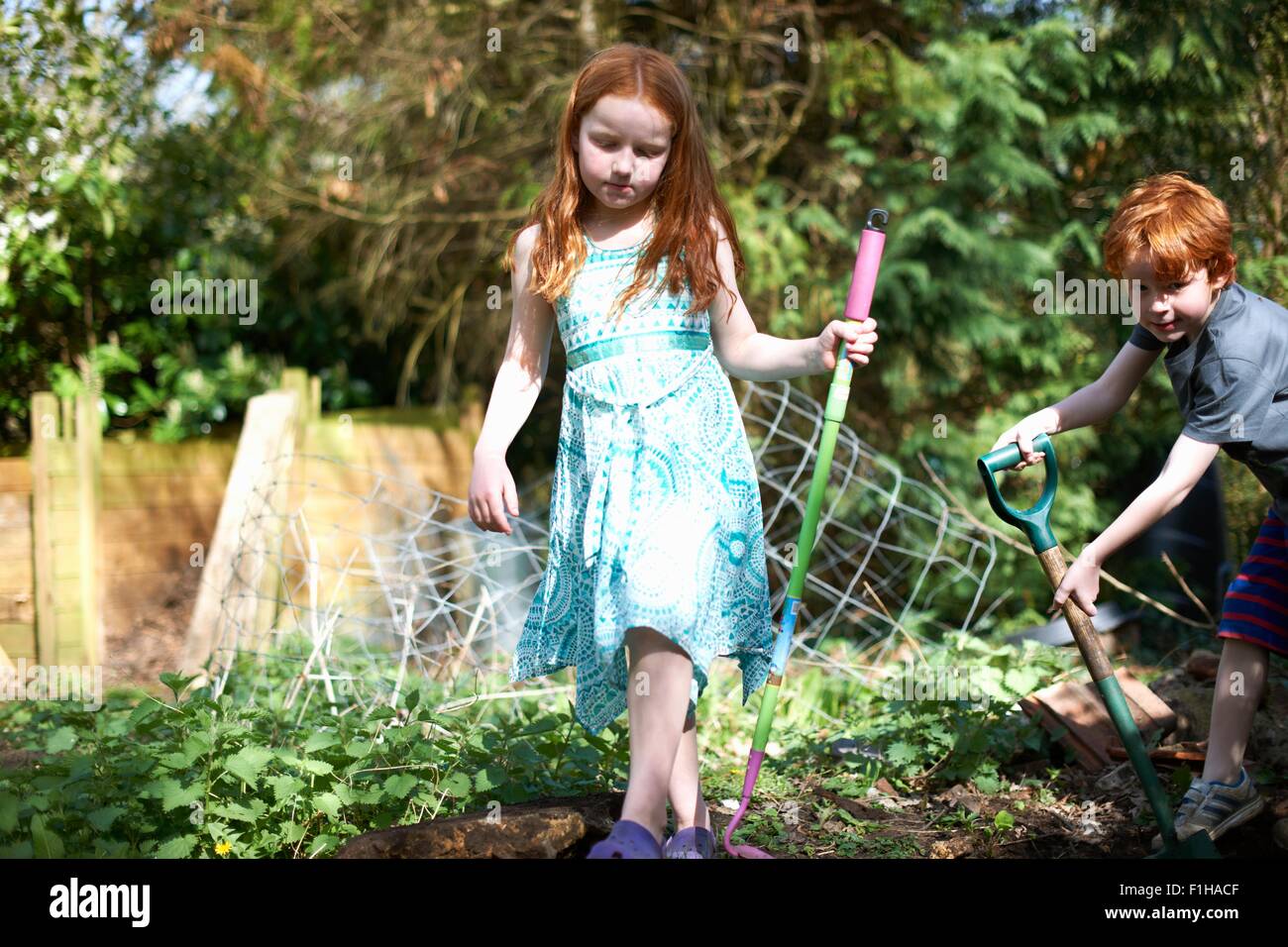 Two young children in garden, holding gardening tools Stock Photo