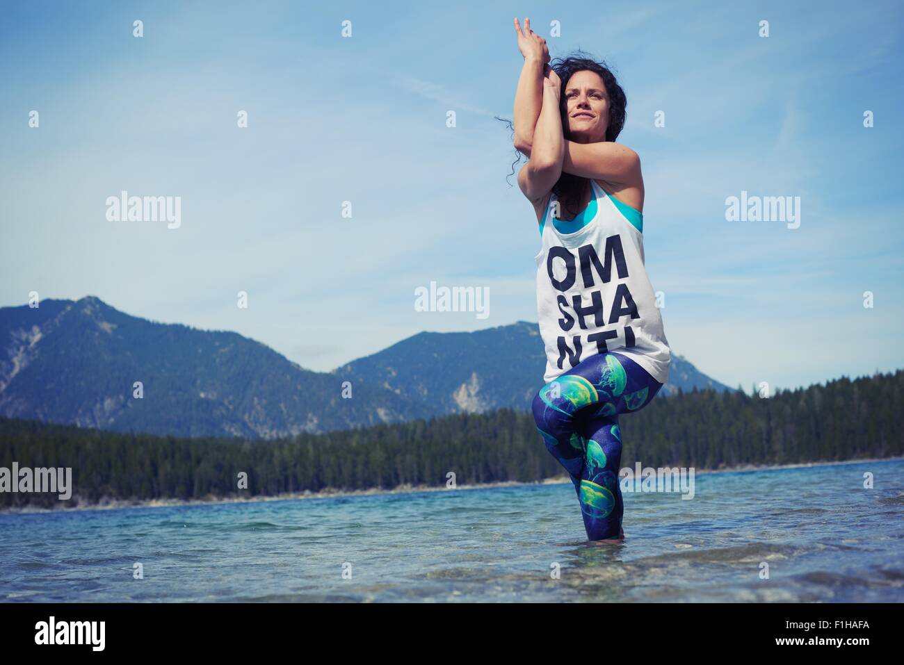 Mid adult woman, standing in lake, in yoga position, low angle view Stock Photo