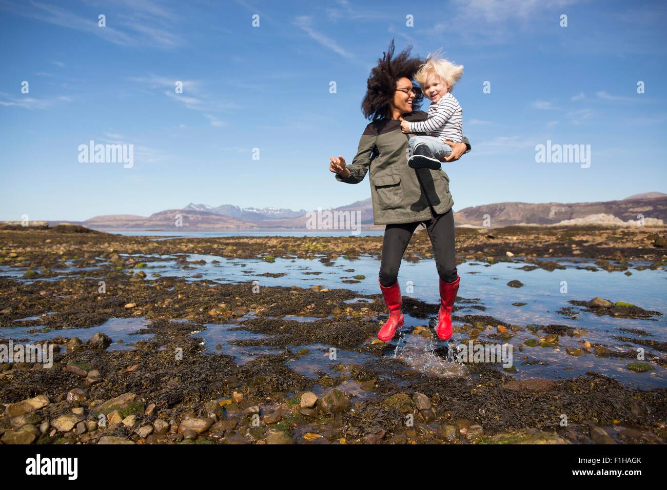 Mother holding son jumping in Loch Eishort, Isle of Skye, Hebrides, Scotland Stock Photo