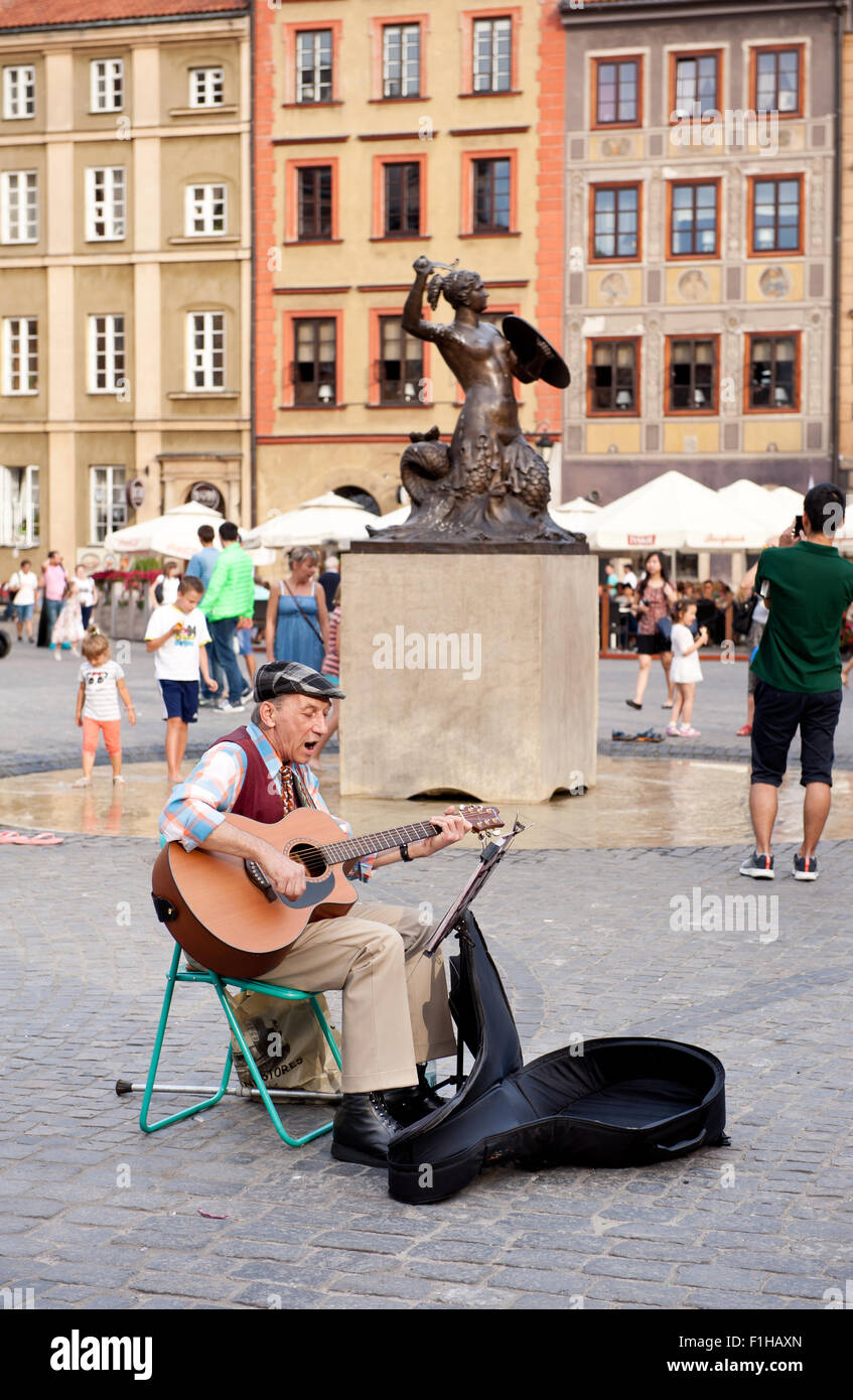 Old man singer gig playing guitar in Old Town Market Place square in Warsaw, Poland. Street art busker performer singing show. Stock Photo