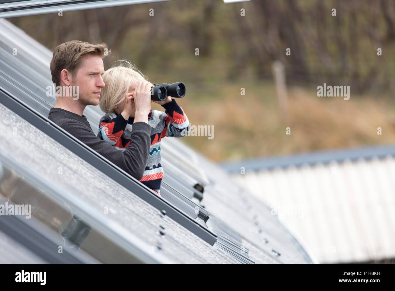 Father and son looking through rooflight, boy using binoculars Stock Photo
