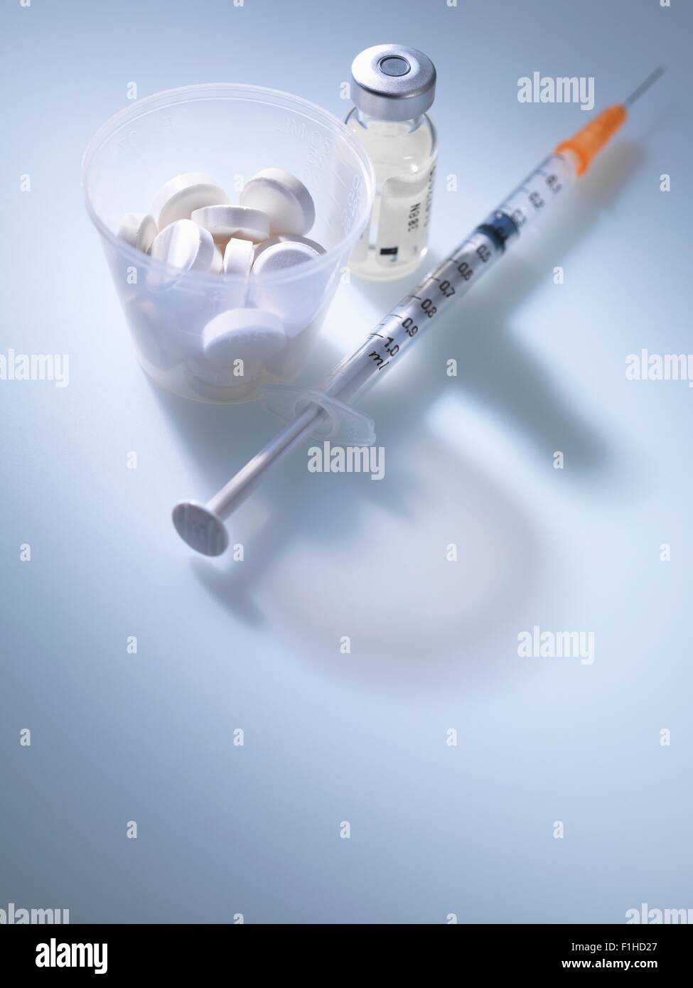 White tablets in plastic measuring cup with vial and syringe Stock Photo